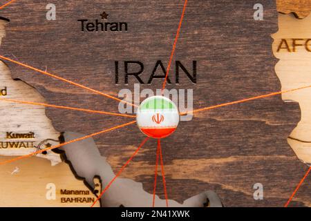 Drapeau de l'Iran sur la punaise et fils rouges sur la carte en bois. Itinéraires de voyage ou logistiques. Influence dans la géopolitique et l'économie mondiale. Banque D'Images