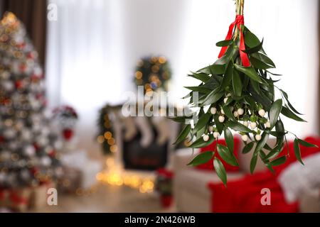 Bouquet de GUI avec ruban rouge suspendu dans la chambre avec arbre de Noël, espace pour le texte Banque D'Images