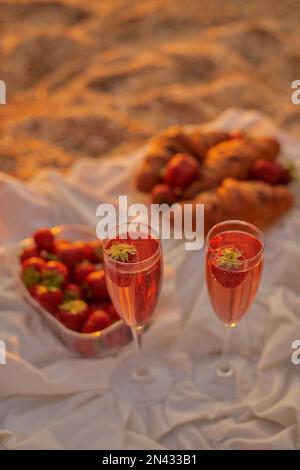 verres de vin rosé avec fraises et croissants pour deux amoureux. pique-nique sur la plage. photo verticale de la vie fixe avec place pour le texte Banque D'Images