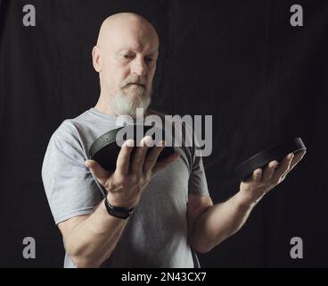 Un homme âgé à tête rasée avec une barbe grise entraîne ses bras avec des haltères. Banque D'Images