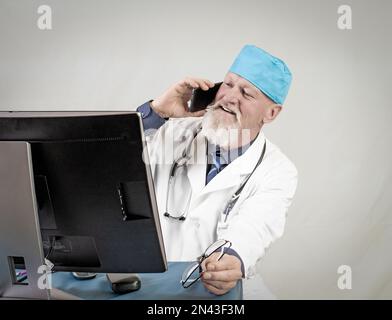 Cabinet médical.médecin âgé positif parlant sur smartphone devant l'ordinateur. Banque D'Images