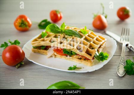 Sandwich de deux omelettes aux œufs avec bacon et tomates à l'intérieur, en forme de gaufre. Banque D'Images