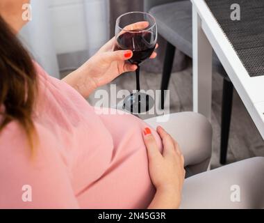 Une fille enceinte avec un gros ventre dans un chemisier rose tient un verre de vin. Le concept de boire de l'alcool pendant la grossesse, une mauvaise habitude. Banque D'Images