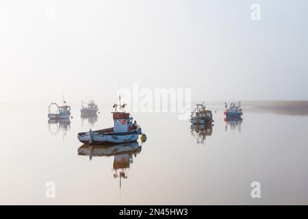 Des bateaux amarrés sur le Ore au large d'Orford Quay dans le Suffolk le matin froid de février tandis que le brouillard et la brume commencent à se dissiper Banque D'Images