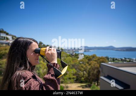 Fille utilisant des jumelles sur un balcon dans une ville à côté de la mer, ville en bord de mer à hobart AUSTRALIE observation des oiseaux Banque D'Images