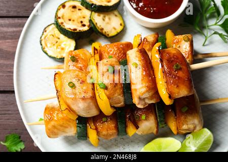 Délicieux kebabs au poulet avec légumes et sauce sur une table en bois, vue du dessus Banque D'Images