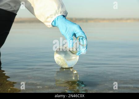 Scientifique avec ballon de florence prenant l'échantillon de la rivière pour analyse, gros plan Banque D'Images