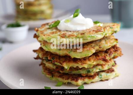 Délicieux beignets de courgettes avec crème aigre dans l'assiette, vue rapprochée Banque D'Images