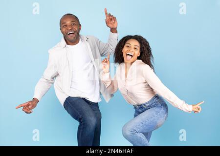 S'amuser ensemble. Joyeux couple noir dansant et se bercer, appréciant la musique préférée sur fond bleu studio Banque D'Images