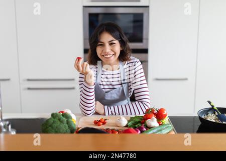 Bonne jolie femme hispanique qui cuisine à la maison, avec des tomates biologiques Banque D'Images