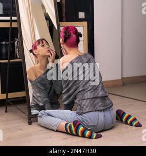 adolescente regarde dans le miroir dans le studio, examine soigneusement son visage Banque D'Images