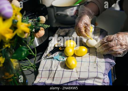 Les mains gantées essorent la peinture du sac sur l'œuf de poulet en vue de pâques. Peinture des oeufs avant les vacances. Préparation de Pâques à Banque D'Images