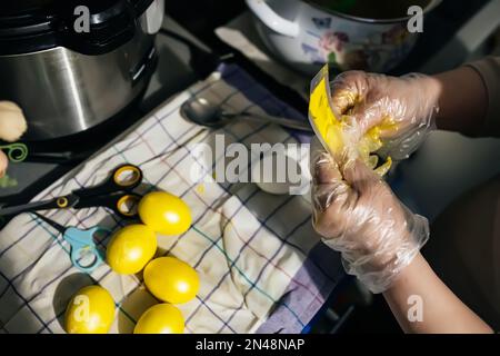 Les mains gantées essorent la peinture du sac sur l'œuf de poulet en vue de pâques. Peinture des oeufs avant les vacances. Préparation de Pâques à Banque D'Images