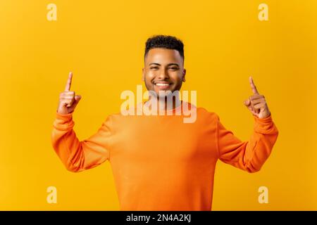 Homme indien attrayant avec une expression faciale surjoyeuse pointant vers le haut avec les deux doigts, présentant l'espace de copie. Studio d'intérieur isolé sur fond jaune Banque D'Images