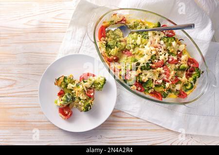 Cocotte de légumes au brocoli, tomates, oignons, feta et fromage, repas sain à base de carb sur une table en bois clair, espace de copie, vue en grand angle Banque D'Images