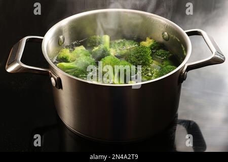Morceaux de brocoli dans un pot de cuisson en acier inoxydable avec de l'eau bouillante et de la vapeur sur une table de cuisson noire, préparer un repas de légumes sain, l'espace de copie, le sele Banque D'Images