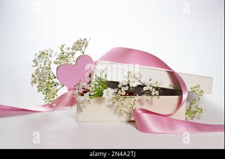 Boîte cadeau avec un coeur peint rose, un ruban et des fleurs de gitsophila blanches comme carte de vœux romantique pour les vacances, fond clair, espace de copie, Banque D'Images
