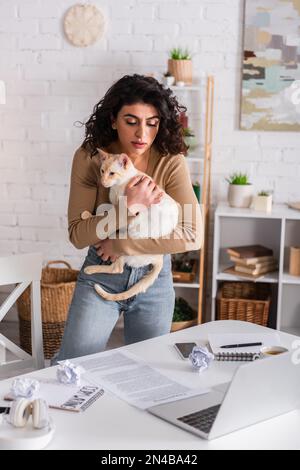 Rédacteur tenant chat oriental près des dispositifs et des documents sur la table, image de stock Banque D'Images