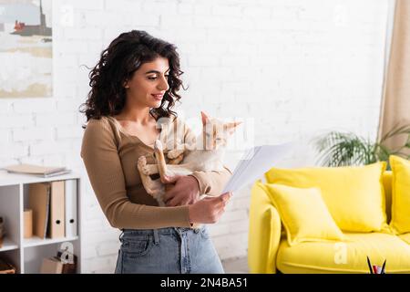 Auteur positif tenant chat oriental et documents à la maison, image de stock Banque D'Images