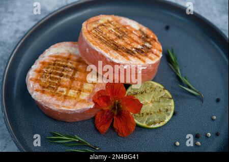 Rouleau de saumon grillé avec mozzarella. Décoration avec vert citron vert et fleurs comestibles Banque D'Images