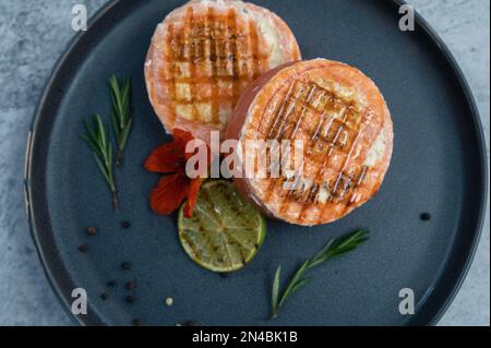 Rouleau de saumon grillé avec mozzarella. Décoration avec vert citron vert et fleurs comestibles Banque D'Images