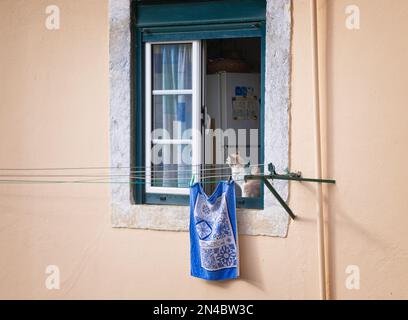 Cat se trouve dans la fenêtre de la cuisine de la maison dans le quartier historique de Mouraria à Lisbonne, Portugal avec une serviette bleue sur la corde à linge Banque D'Images