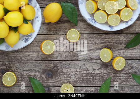 Cadre décoratif citronné ou bordure sur fond de bois, arrangée de fruits entiers, coupés en deux et tranchés sur des assiettes avec des feuilles, vue sur le dessus de la table. Banque D'Images