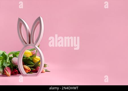 Statuette de lapin de pâques en bois et tulipes de printemps sur fond rose, concept minimal de pâques avec espace de copie Banque D'Images