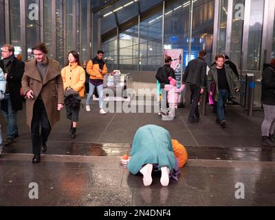 Un homme sans domicile imploré pour de l'argent comptant prostrate sur un sol humide, devant la station de métro très fréquentée dans le centre de Londres Banque D'Images