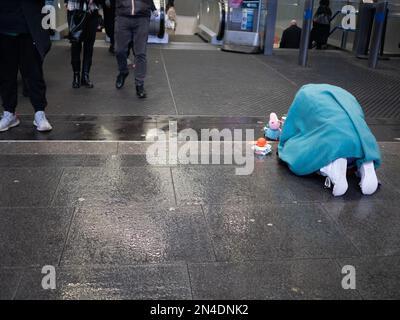 Un homme sans domicile imploré pour de l'argent comptant prostrate sur un sol humide, devant la station de métro très fréquentée dans le centre de Londres Banque D'Images