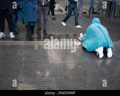 Un homme sans domicile imploré pour de l'argent comptant prostrate sur un sol humide, devant la station de métro très fréquentée dans le centre de Londres Banque D'Images