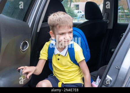 Portrait d'un garçon souriant avec un sac d'école sortant de la voiture. Prendre un étudiant après l'école. Le garçon entre dans la voiture. Banque D'Images