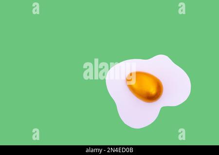 Décor créatif composé d'œufs brouillés et d'œufs de Pâques dorés sur fond vert. Concept de vacances de printemps minimales. Banque D'Images