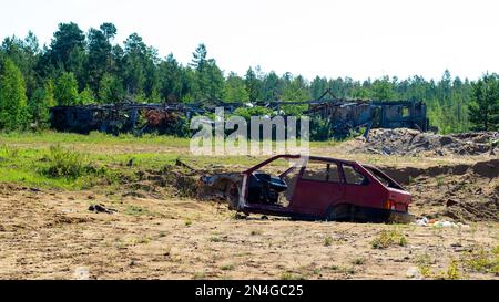 Abandonné brûlé le corps d'une vieille voiture russe dans le champ sur le fond de abandonné après les bâtiments de ferme d'incendie dans les bois dans l'af Banque D'Images