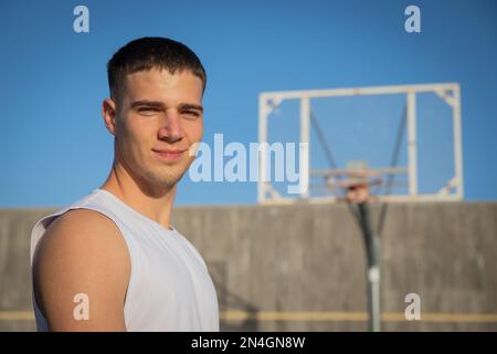 Un joueur de basket-ball souriant sur un terrain de basket-ball avec un panier derrière lui. Banque D'Images