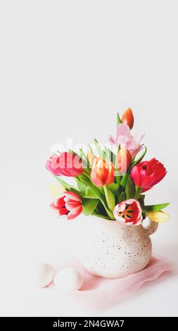 Pâques reste la vie avec des tulipes multicolores dans une carafe et des œufs blancs sur fond blanc avec espace de copie. Préparation pour Pâques. Ambiance de vacances de printemps. Ver Banque D'Images