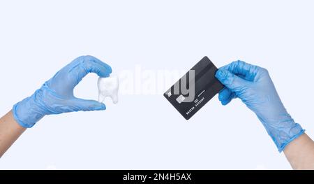 La main de dentiste femelle dans des gants bleus tient le modèle de dent de dentiste et la carte de crédit. Arrière-plan clair. Concept du coût du traitement dentaire Banque D'Images