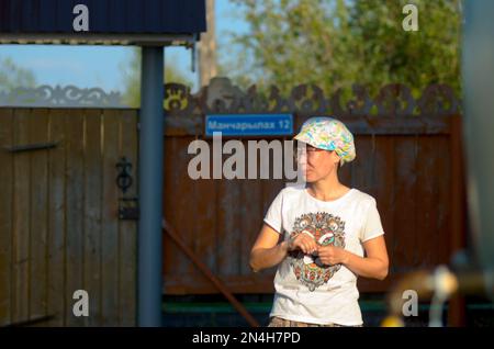 Sourire Yakut fille dans un t-shirt et Cap est sur un quartier résidentiel d'une maison privée dans le village nord de la Russie. Banque D'Images