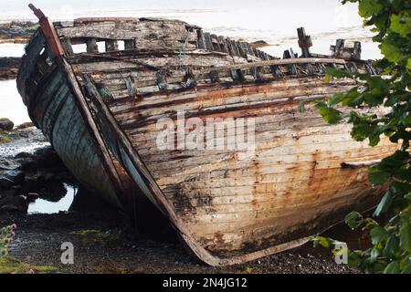 La coque deux long navire en bois pendu d'un côté, en décomposition et pourriture dans le bord de l'eau peu profonde à Salen, Mull, Écosse Banque D'Images