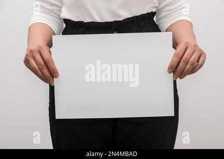 Les mains des femmes tiennent une feuille de papier vierge isolée sur un fond blanc. Banque D'Images