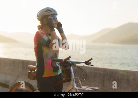 Femme cycliste asiatique portant des lunettes de soleil se préparer pour une promenade matinale en vélo autour du lac avec belle vue sur la montagne en arrière-plan. Banque D'Images