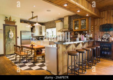 Cuisine avec armoires blanches et brunes, comptoirs en quartz, table et bancs en bois anciens, comptoir en acier inoxydable dans une luxueuse maison de campagne. Banque D'Images