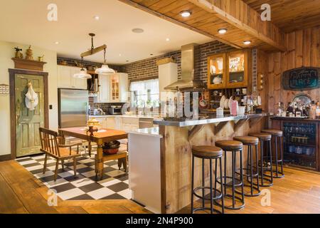 Cuisine avec armoires blanches et brunes, comptoirs en quartz, table et bancs en bois anciens, comptoir en acier inoxydable dans une luxueuse maison de campagne. Banque D'Images