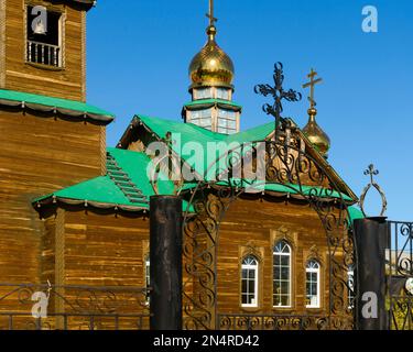 Croix de métal sur la clôture à l'entrée de l'église orthodoxe avec des dômes et des crucifix en bois dans le village de Suntar de Yakut du nord. Banque D'Images