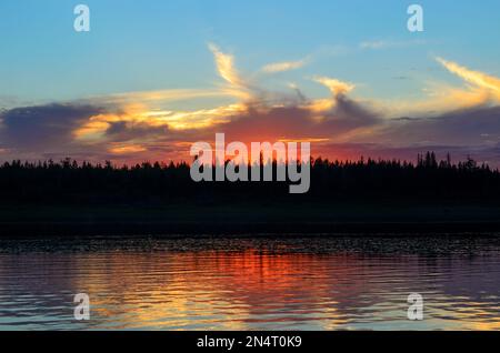 Coucher de soleil orange vif derrière les nuages de soleil sur les rives de la rivière Viluy Nord sous le ciel bleu dans la forêt d'épicéa et la silhouette d'un Banque D'Images