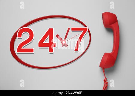 service d'assistance téléphonique 24h/24/7, 7j Combiné rouge sur fond gris clair, vue du dessus Banque D'Images