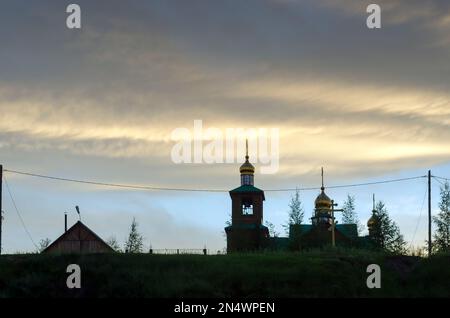 Une église en bois avec des dômes d'or se dresse au coucher du soleil sous le ciel gras sur une colline dans le village nord de Yakutia suntar. Banque D'Images