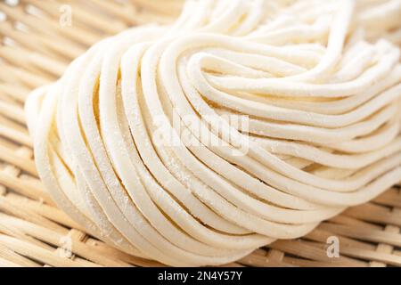 Nouilles udon fraîches dans une passoire de bambou placée sur un fond blanc. Nouilles Udon avant ébullition. Nouilles udon fraîchement préparées. Banque D'Images