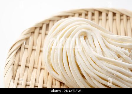 Nouilles udon fraîches dans une passoire de bambou placée sur un fond blanc. Nouilles Udon avant ébullition. Nouilles udon fraîchement préparées. Banque D'Images