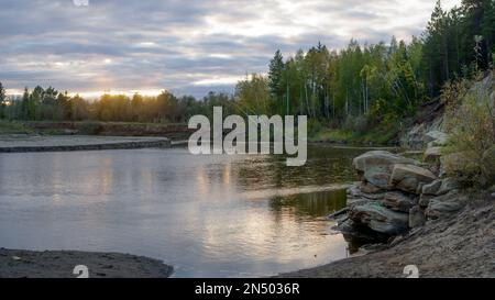 Coucher de soleil lumineux avec réflexion dans l'eau d'une petite rivière Kempendyay à Yakutia entre les falaises et les forêts d'épicéa dans le nord sauvage. Banque D'Images